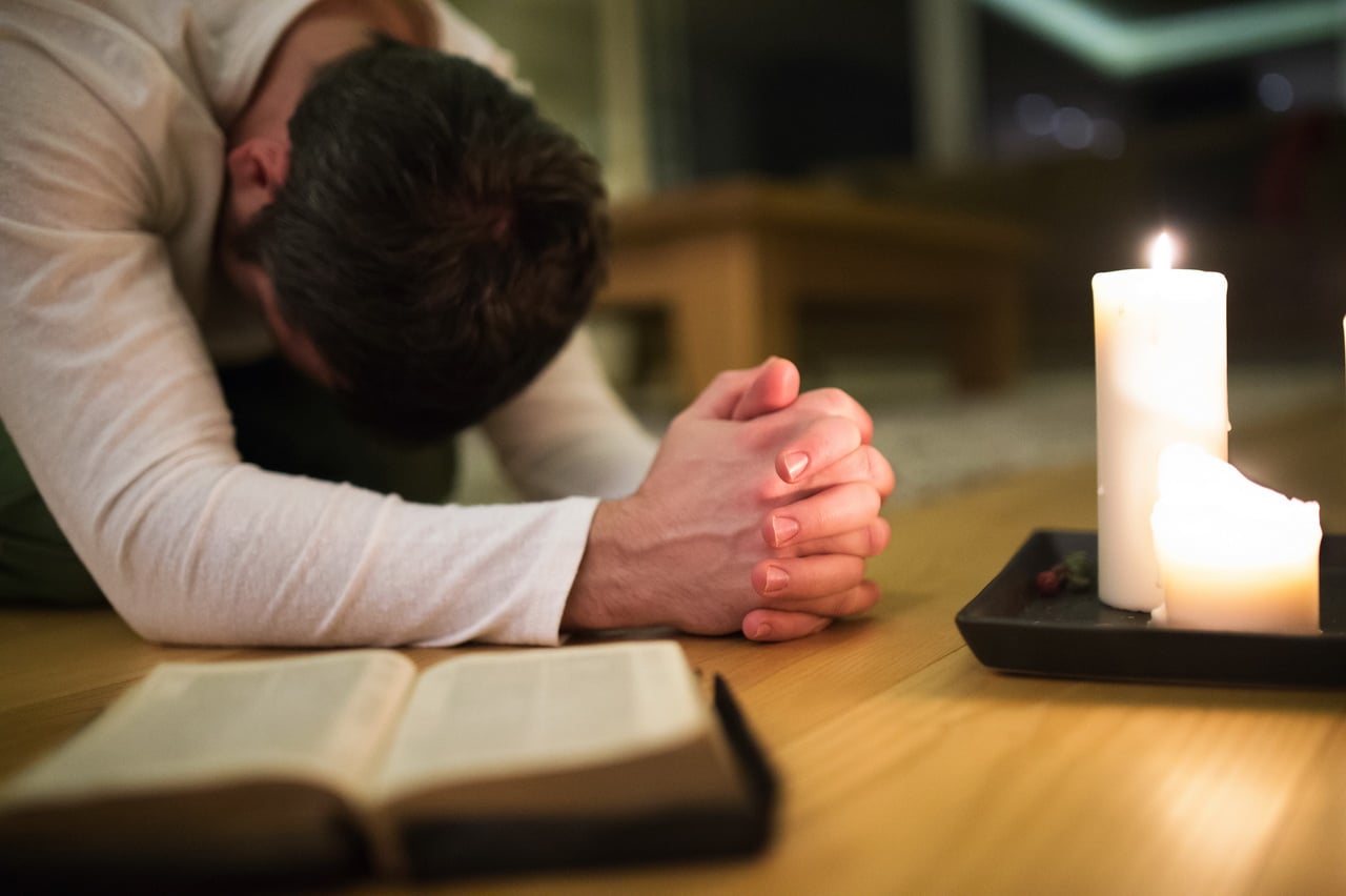 Young Man Praying, Kneeling, Bible And Candle Next To Him.