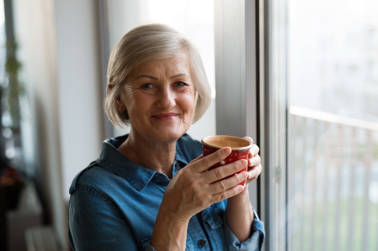 Senior Woman At The Window Holding A Cup Of Coffee